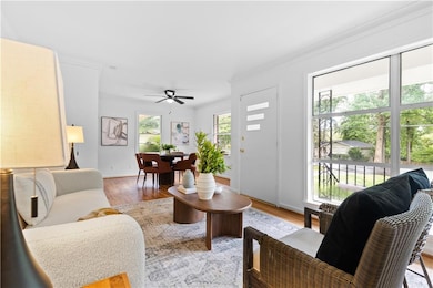 Living room with crown molding, light wood-type flooring, baseboards, and ceiling fan