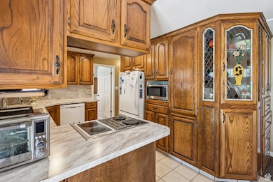Kitchen with light countertops, white appliances, brown cabinets, and light tile patterned floors