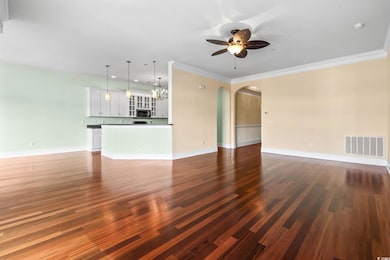 Unfurnished living room with dark wood-type flooring, ceiling fan, arched walkways, crown molding, and a chandelier