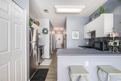 Kitchen with appliances with stainless steel finishes, a sink, light wood-style floors, white cabinets, and a peninsula