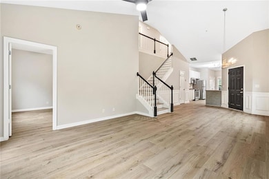 Unfurnished living room with stairway, a ceiling fan, light wood finished floors, and high vaulted ceiling