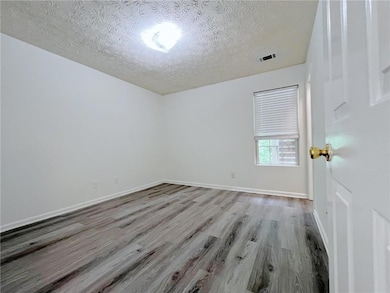Empty room with a textured ceiling, wood finished floors, and baseboards