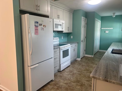Kitchen featuring white appliances, backsplash, and dark stone countertops