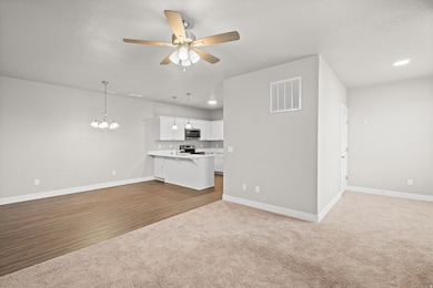 Unfurnished living room with dark carpet, a chandelier, a ceiling fan, and dark wood-style flooring