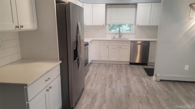 Kitchen with stainless steel appliances, white cabinets, tasteful backsplash, and light wood-style floors