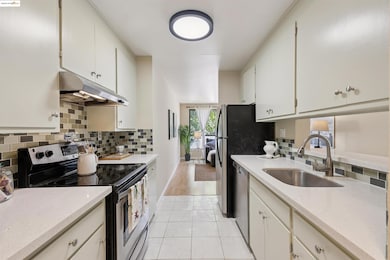 Kitchen with stainless steel appliances, light stone countertops, under cabinet range hood, backsplash, and light tile patterned floors