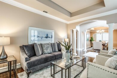 Living room featuring crown molding, decorative columns, a tray ceiling, hand-scraped hardwood floors, and an inviting chandelier