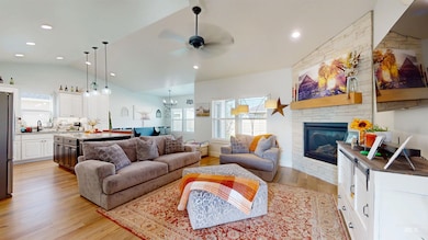 Living area featuring light wood-type flooring, lofted ceiling, ceiling fan, a stone fireplace, and recessed lighting