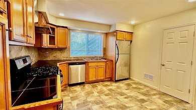 Kitchen with stainless steel appliances, glass insert cabinets, tasteful backsplash, wall chimney exhaust hood, and brown cabinets