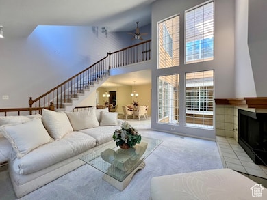 Carpeted living room featuring a fireplace with raised hearth, ceiling fan, a towering ceiling, a chandelier, and stairs