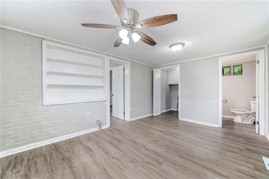 Unfurnished bedroom with brick wall, wood finished floors, baseboards, a textured ceiling, and ensuite bathroom