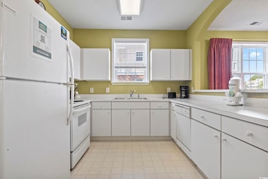 Kitchen featuring white appliances, white cabinets, light countertops, a textured ceiling, and light flooring