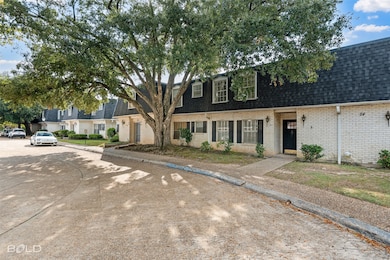 View of front of property with a shingled roof, brick siding, and mansard roof