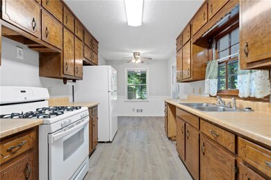 Kitchen featuring white gas range, light wood-style flooring, light countertops, ceiling fan, and brown cabinetry
