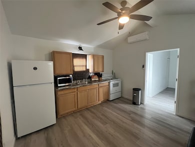 Kitchen featuring white appliances, light wood finished floors, a ceiling fan, tasteful backsplash, and an AC wall unit