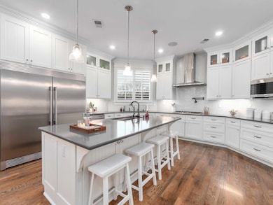 Kitchen featuring wall chimney exhaust hood, appliances with stainless steel finishes, white cabinets, a sink, and dark wood-style floors