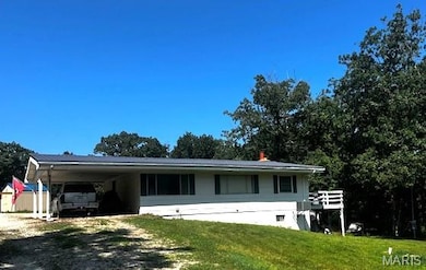 View of front of house featuring gravel circle driveway, a carport, a front lawn, and a shed