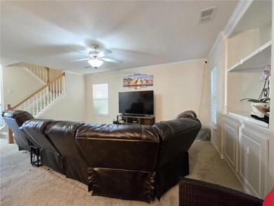 Living room featuring light colored carpet, ornamental molding, ceiling fan, stairs, and a textured ceiling