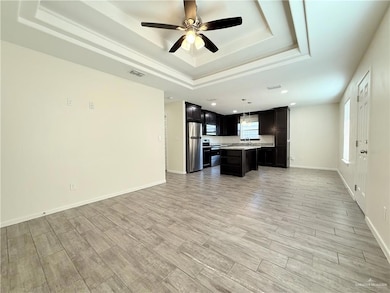 Unfurnished living room with a tray ceiling, ceiling fan, light wood-style flooring, recessed lighting, and baseboards