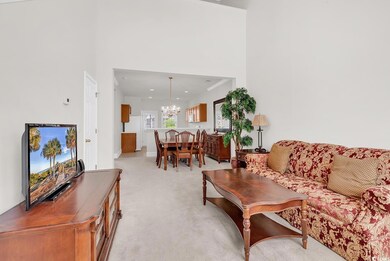 Living area featuring a chandelier, light colored carpet, a towering ceiling, and baseboards