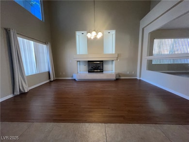 Unfurnished living room with a high ceiling, wood finished floors, a glass covered fireplace, and a chandelier