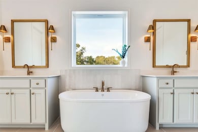 Full bath with two vanities, a freestanding tub, light tile patterned floors, tile walls, and a wainscoted wall