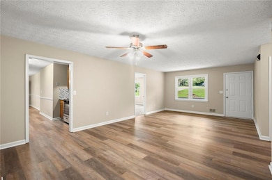 Empty room with a ceiling fan, a textured ceiling, and wood finished floors