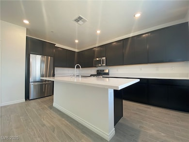 Kitchen with dark cabinets, light wood-style flooring, appliances with stainless steel finishes, recessed lighting, and a center island with sink