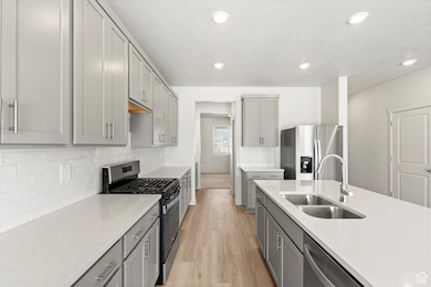 **DISCLAIMER - some exterior and interior options may vary**Kitchen with gray cabinetry, stainless steel appliances, light stone countertops, light wood finished floors, and decorative backsplash