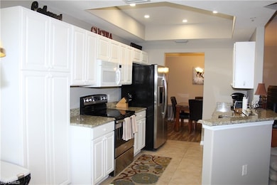 Kitchen with light hardwood / wood-style floors, range with electric stovetop, white cabinetry, and a raised ceiling