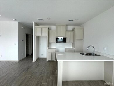 Kitchen featuring visible vents, a sink, stainless steel microwave, a peninsula, and dark wood-style flooring