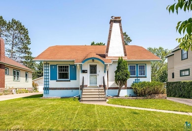 View of front of property featuring a chimney, a front lawn, stucco siding, and roof with shingles