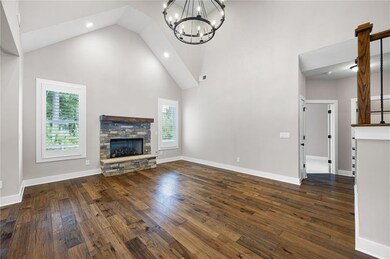 Unfurnished living room featuring high vaulted ceiling, a chandelier, wood finished floors, a stone fireplace, and recessed lighting