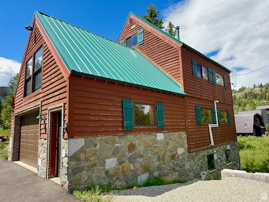 View of property exterior featuring asphalt driveway, stone siding, a metal roof, and a garage