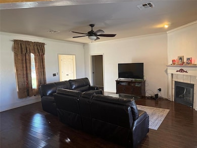 Living room with dark wood finished floors, ornamental molding, a tile fireplace, and a ceiling fan