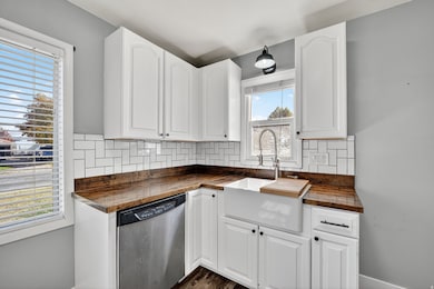 Kitchen featuring tasteful backsplash, stainless steel dishwasher, white cabinetry, and wooden counters