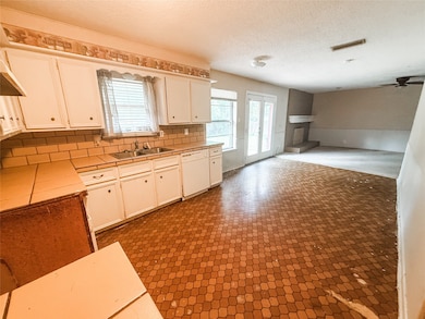 Kitchen featuring white dishwasher, tile countertops, white cabinets, a ceiling fan, and backsplash