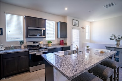 Kitchen with stainless steel appliances, light stone counters, a breakfast bar area, a kitchen island with sink, and light tile patterned flooring