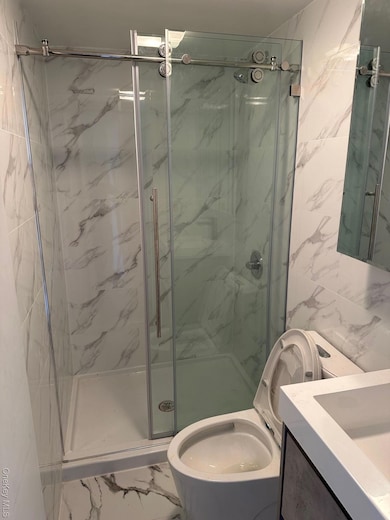 Bathroom featuring marble finish floors, tile walls, vanity, and a marble finish shower