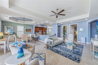 Living room with a raised ceiling, arched walkways, ceiling fan, light tile patterned flooring, and recessed lighting