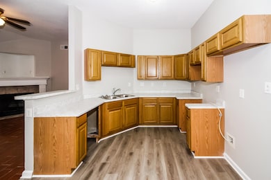 Kitchen with light wood-style floors, ceiling fan, a tiled fireplace, a peninsula, and light countertops