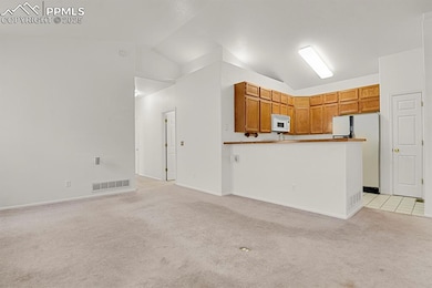 Kitchen fwith all appliances, vaulted ceiling, light carpet, brown cabinetry, and open floor plan