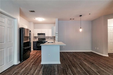 Kitchen featuring black appliances, under cabinet range hood, dark wood-style floors, a peninsula, and white cabinets