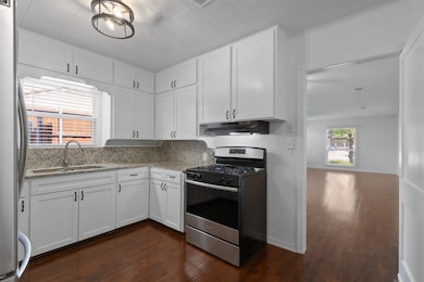 Kitchen with stainless steel appliances, white cabinetry, dark wood finished floors, and light stone countertops
