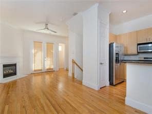 Kitchen featuring stainless steel appliances, light wood-style flooring, light brown cabinets, dark countertops, and a glass covered fireplace