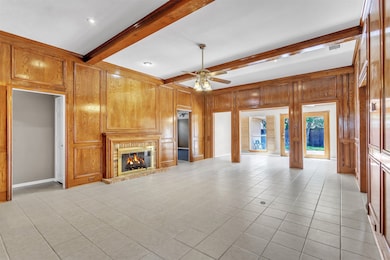 Unfurnished living room with beam ceiling, light tile patterned floors, a fireplace, a ceiling fan, and wooden walls