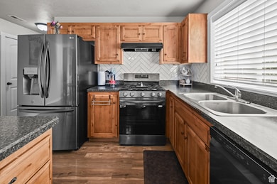 Kitchen with refrigerator with ice dispenser, stainless steel gas range, black dishwasher, backsplash, and dark wood-style floors