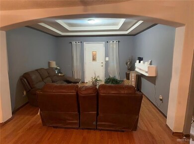 Living area featuring a raised ceiling, arched walkways, and light wood-style flooring