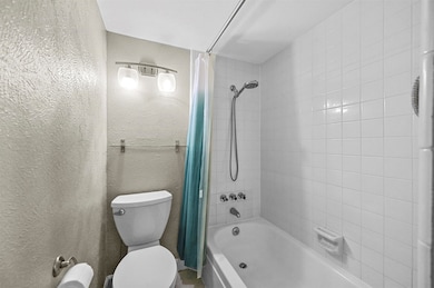 Bathroom featuring shower / bathtub combination with curtain and a textured wall
