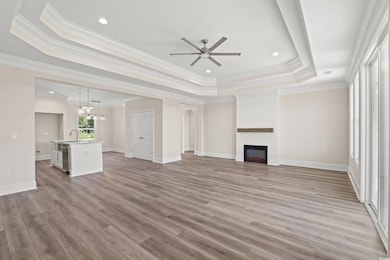 Unfurnished living room with a tray ceiling, ceiling fan, crown molding, a fireplace, and light wood-type flooring